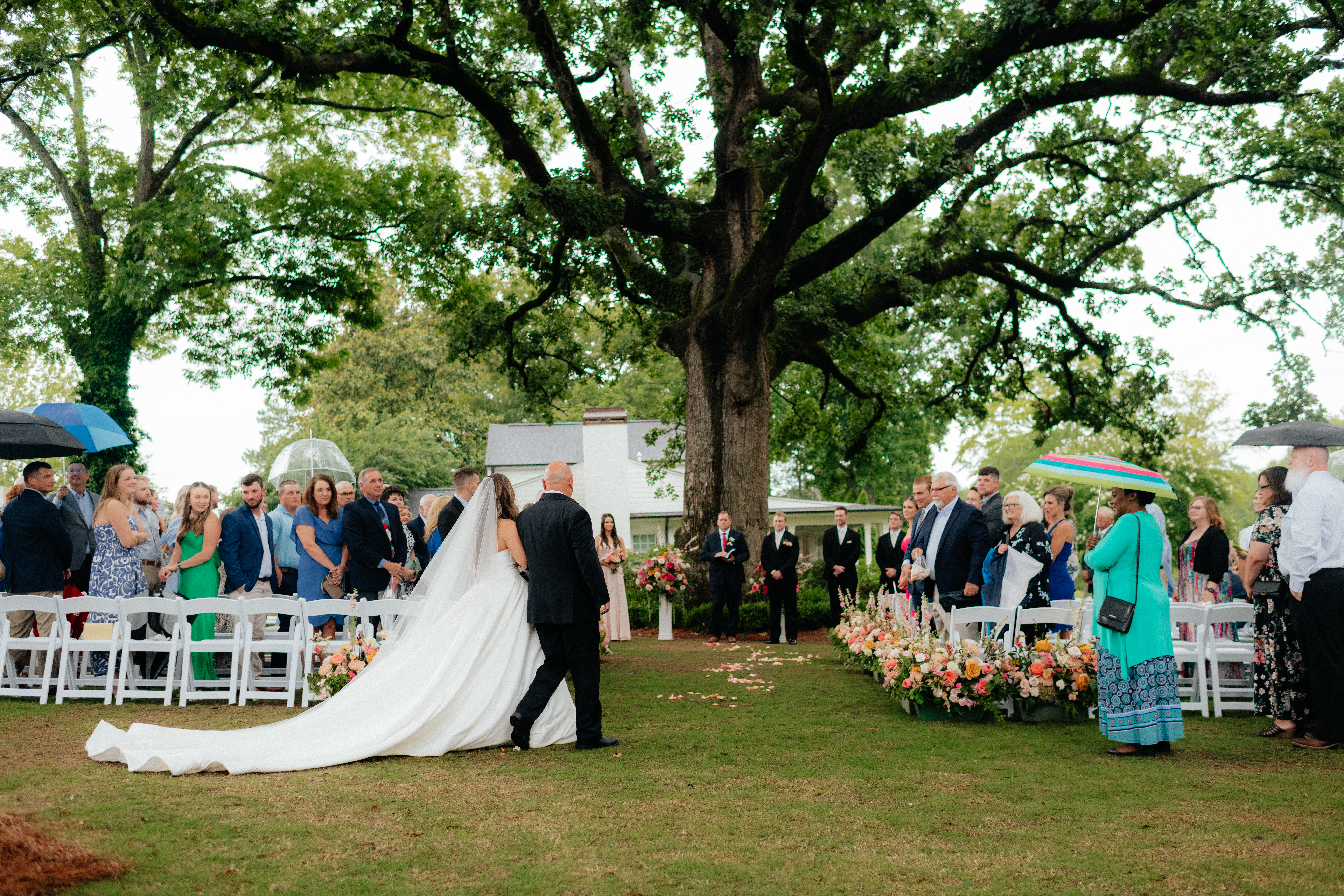a rainy summer wedding ceremony at the live oak in the backyard of the lumpkin house wedding venue, albertville, alabama