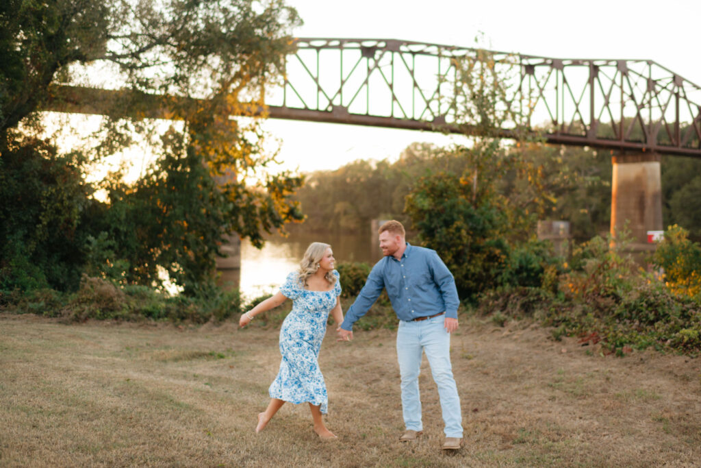 a couple in an all blue engagement photo outfit runs along the river during their session with washington and alabama engagement photographer sarah mismash