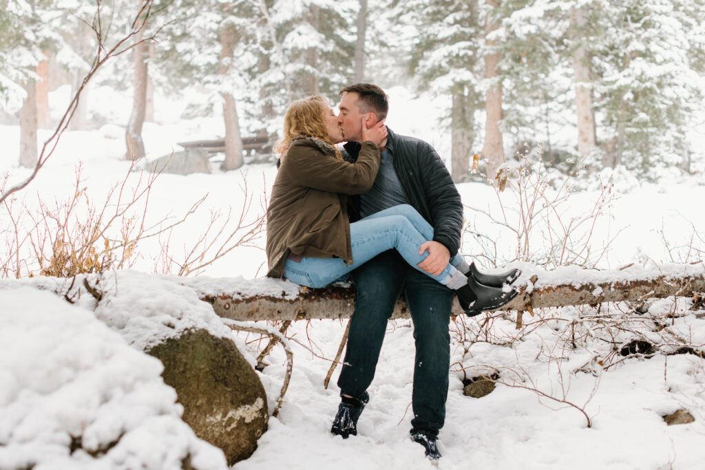 a couple sits on a snow covered log together during their winter engagement photos with olympia wedding photographer sarah mismash