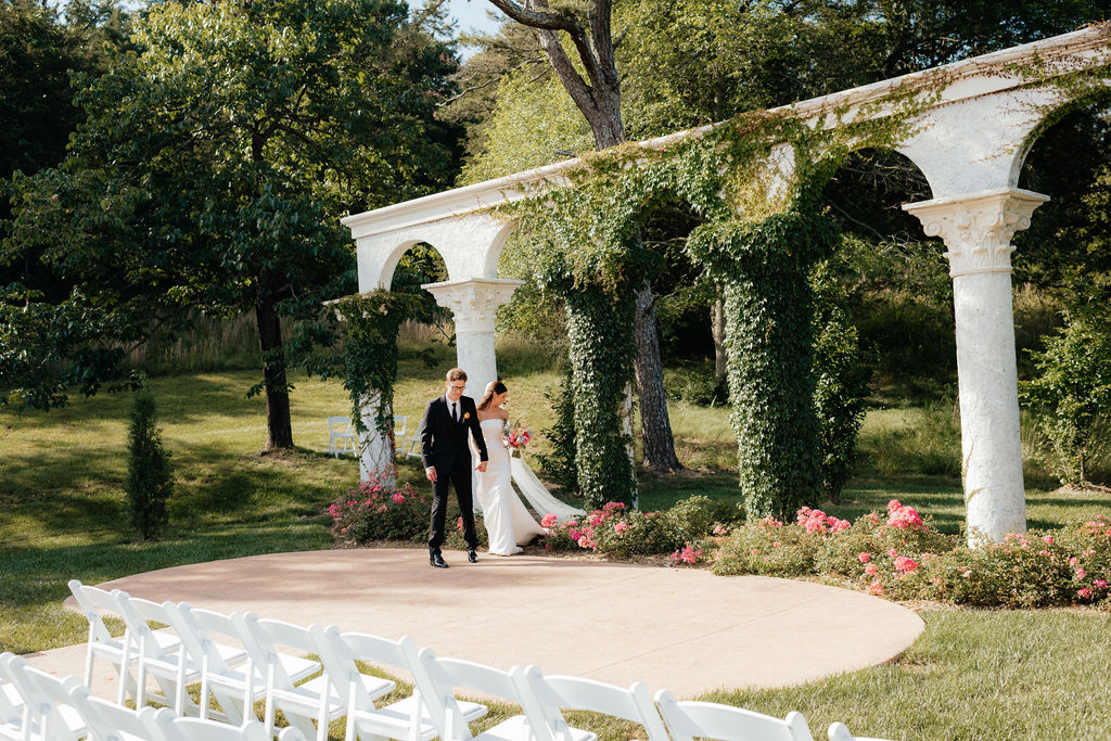 a bride and groom walk past ivy covered columns, their ceremony site at howe farms, their wedding venue in chattanooga tn