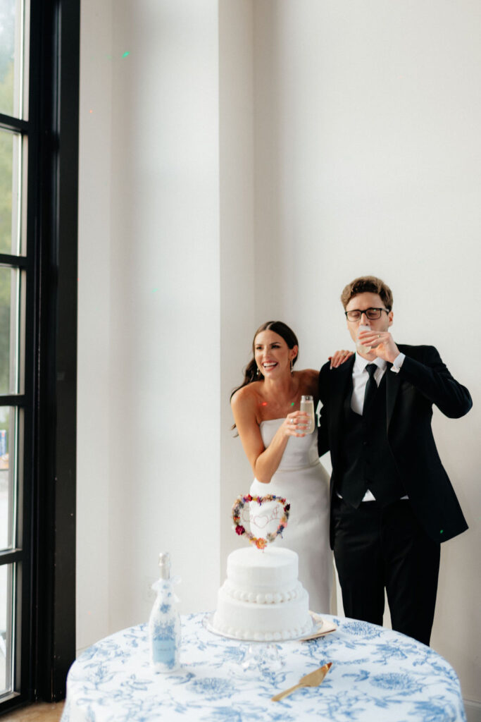 a bride laughs while her husband takes a sip of a drink during their cake cutting at howe farms wedding venue in chattanooga, tn