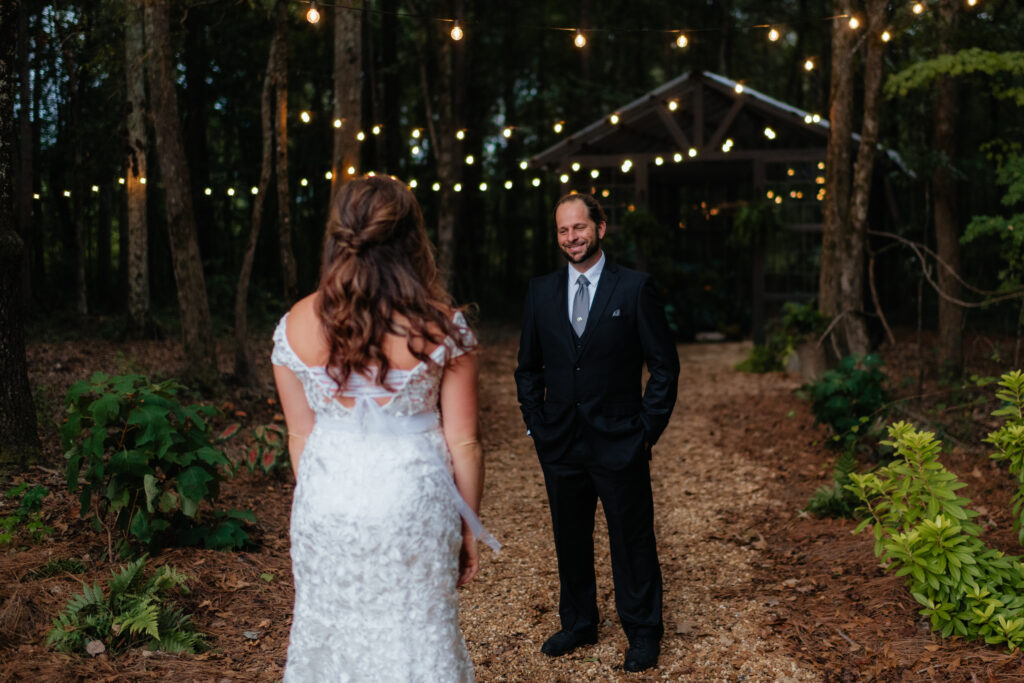 a groom smiles at his bride during their first look at the glasshouse alabama eden with alabama wedding photographer Sarah Mismash