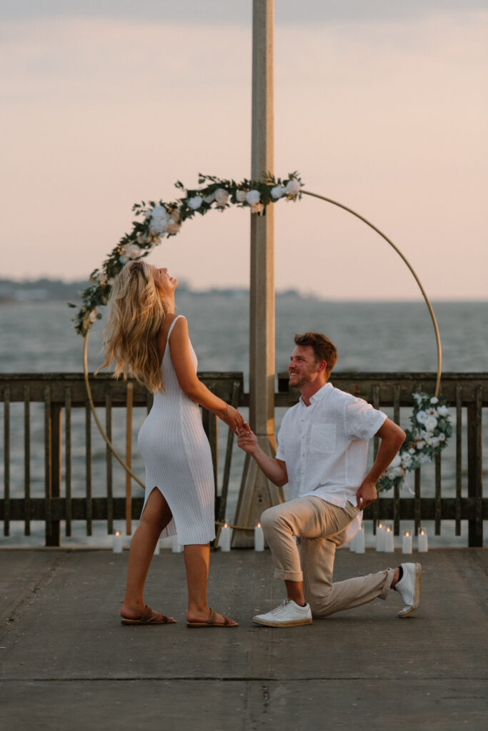 Man proposes on bended knee during a surprise proposal at Fairhope Municipal Pier, Alabama. Photos taken by Sarah Mismash Photography