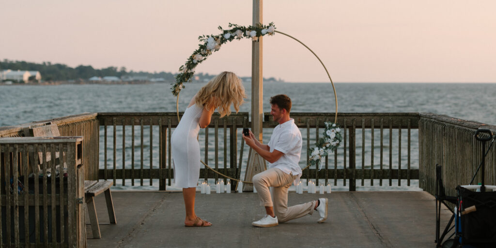 Man proposes on bended knee during a surprise proposal at Fairhope Municipal Pier, Alabama. Photos taken by Sarah Mismash Photography
