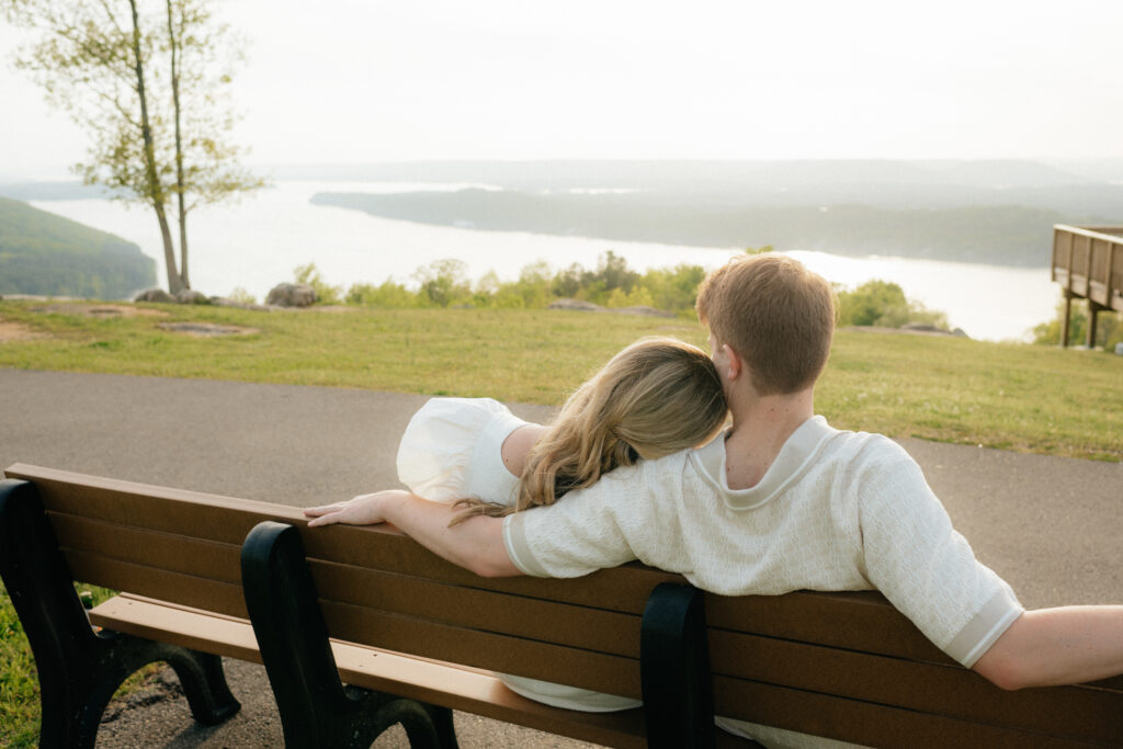 a couple watches the sunset on a bench over guntersville lake at weathington park in north Alabama during their engagement photos at weathington park in skyline, alabama