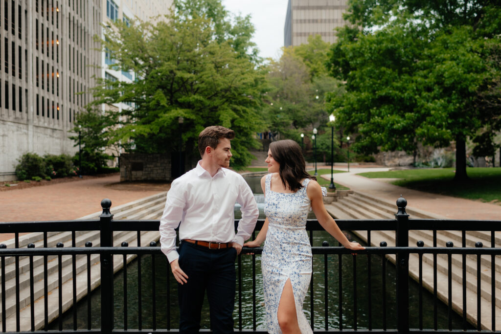 a couple pauses on the bridge over the big spring canal during their urban spring engagement photos in downtown huntsville with alabama wedding photographer Sarah Mismash