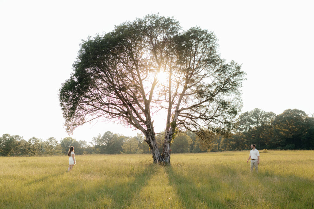 a couple stops by a large oak tree during their summer field engagement photos in calera, alabama, photography by Birmingham alabama wedding photographer Sarah Mismash