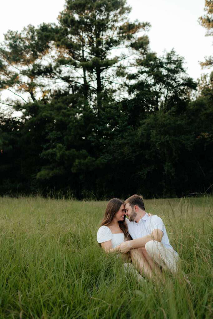 a couple sits in the grass during their summer field engagement photos in calera, alabama, photography by Birmingham alabama wedding photographer Sarah Mismash