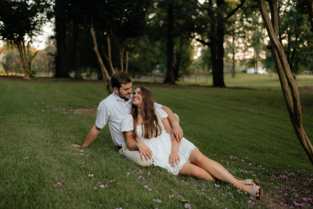 a couple pauses in the grass under the crepe myrtles during their summer field engagement photos in calera, alabama, photography by Birmingham alabama wedding photographer Sarah Mismash