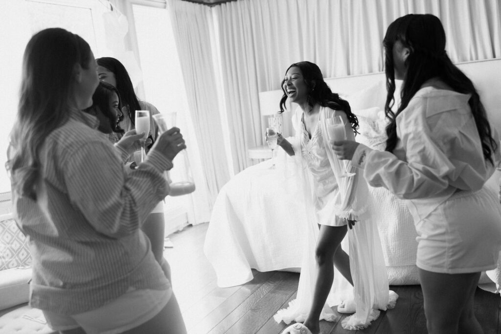 a bride laughs with her bridesmaids over champagne while they prepare for the wedding day on lake Martin with alabama wedding photographer Sarah Mismash