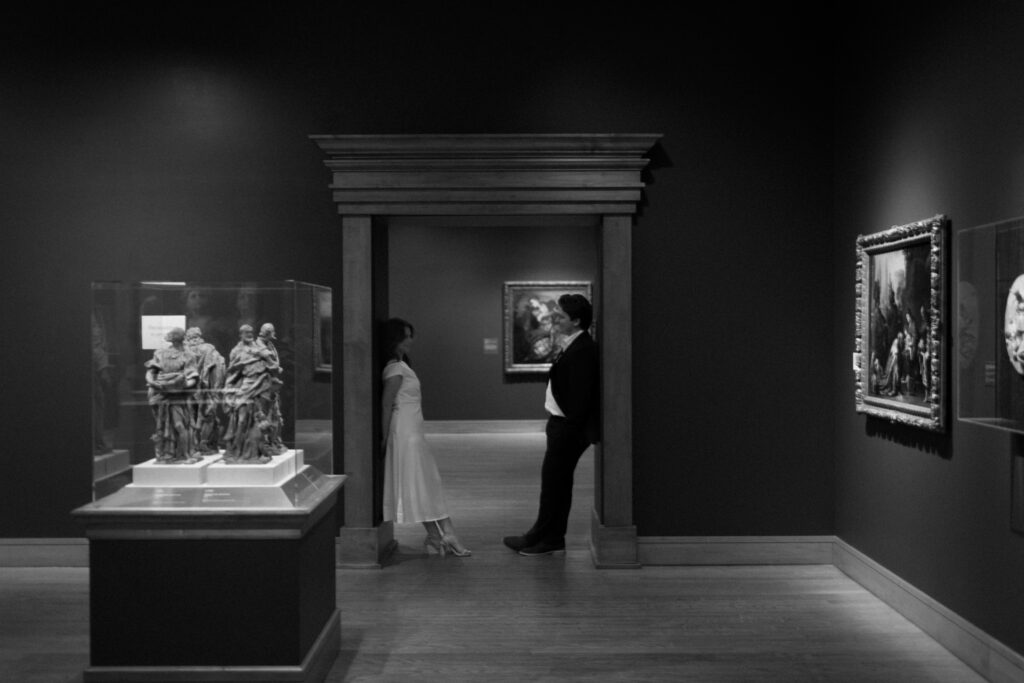 a couple stands in the doorway between exhibits at the Birmingham museum of art during their engagement photos with alabama wedding photographer Sarah Mismash