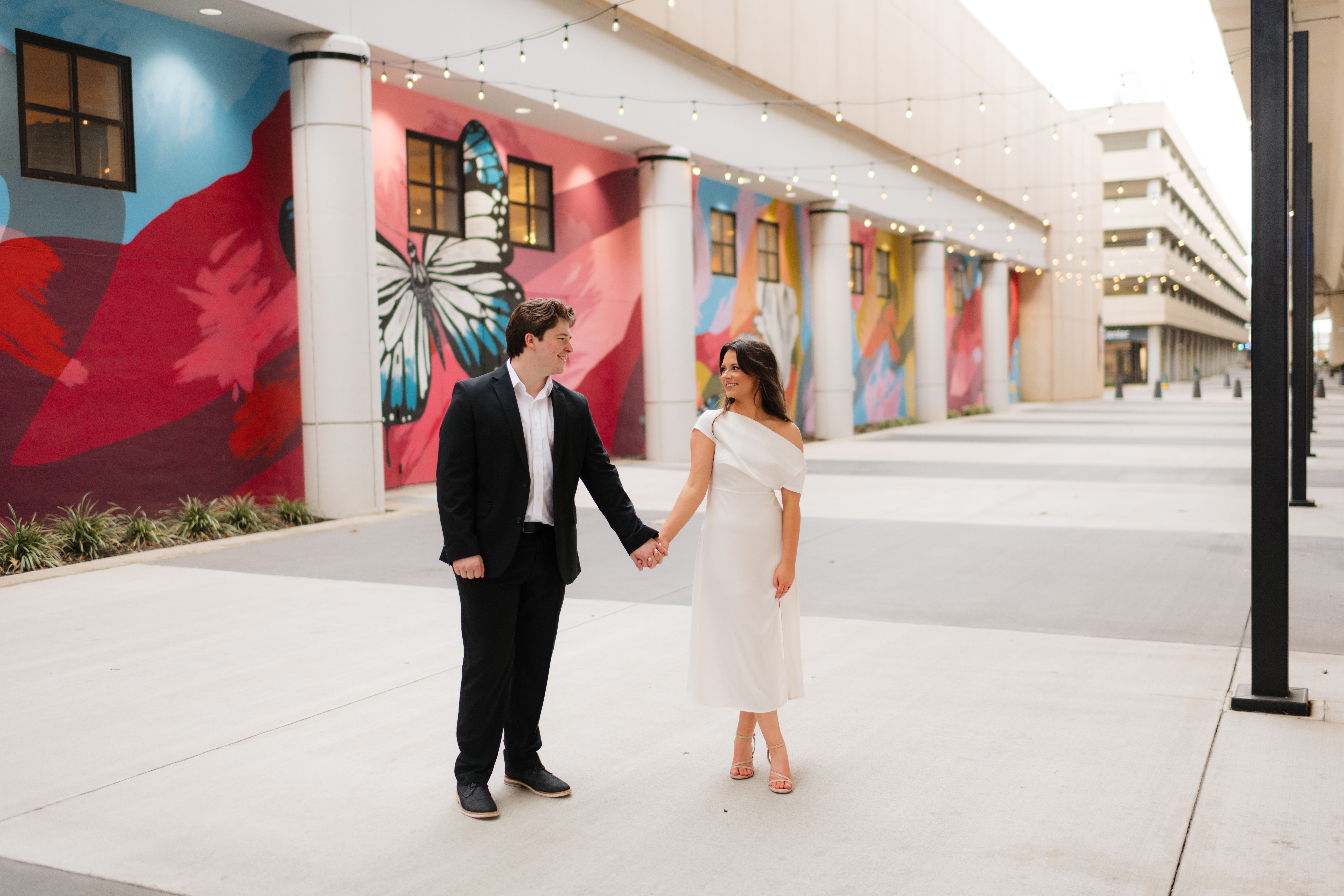 a couple pauses under the lights near a mural near the bham city walk and Birmingham museum of art during their urban downtown engagement photos with alabama wedding photographer Sarah Mismash