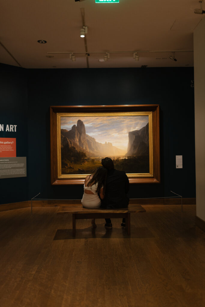 a couple looks at a painting of Yosemite together during their engagement photos at the Birmingham museum of art in downtown bham with alabama wedding photographer Sarah Mismash