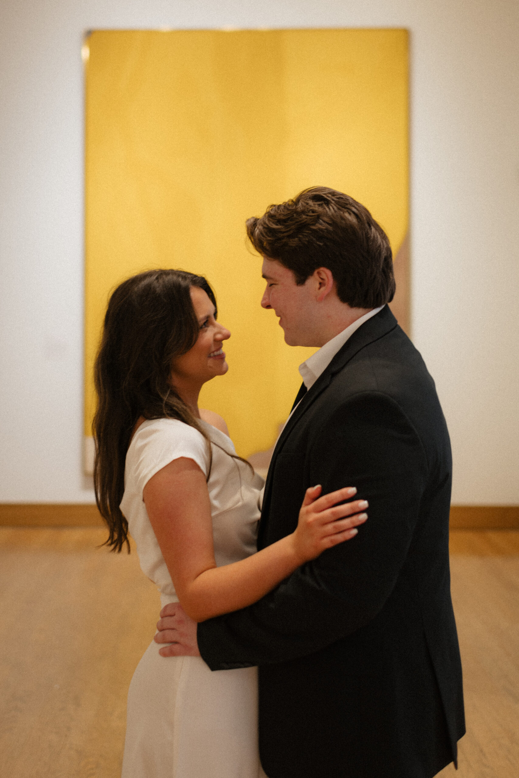 a couple smiles together in front of a yellow painting in the Birmingham museum of art during their indoor engagement photos in downtown Birmingham with alabama wedding photographer Sarah Mismash