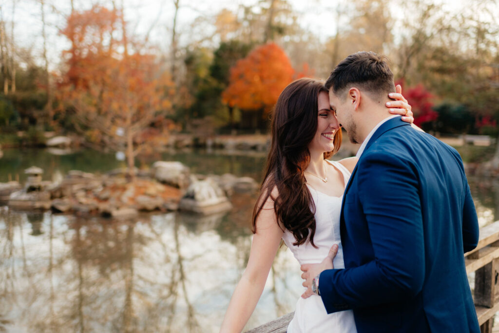 a couple stands on a wooden bridge in the japanese section of the birmingham botanical gardens during a december fall engagement photo session with alabama wedding photographer sarah mismash