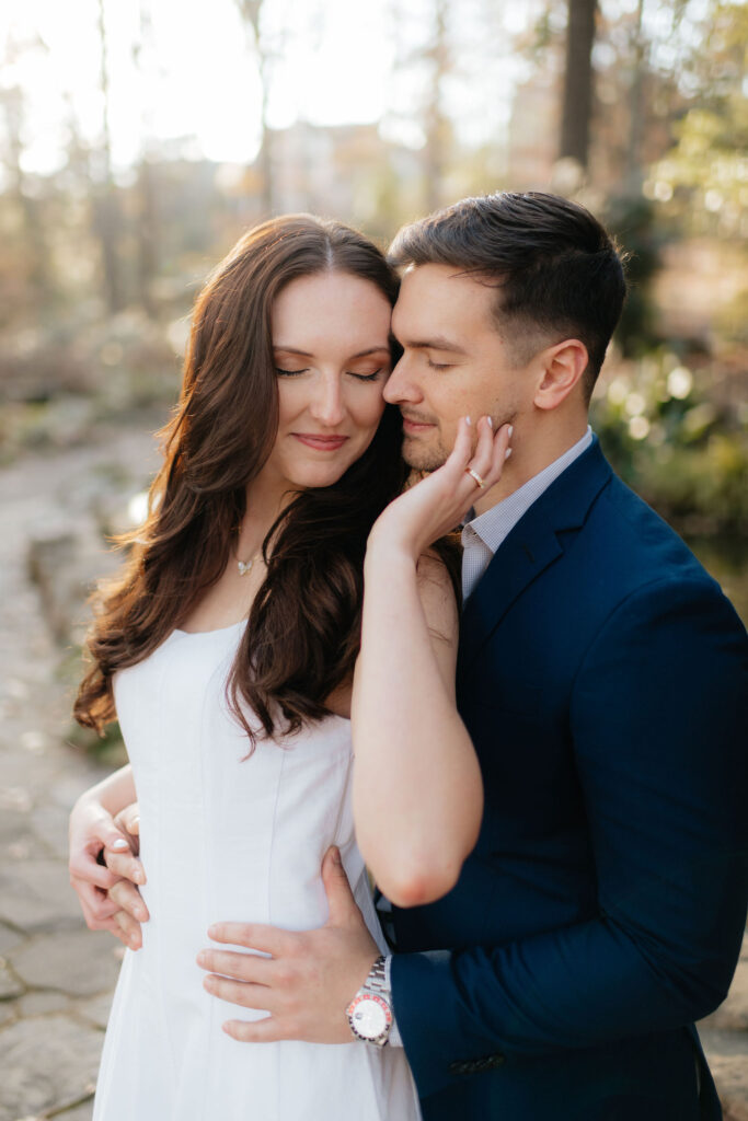 a couple holds each other near a small waterfall at the birmingham botanical gardens in december, during their engagement photos with alabama wedding photographer sarah mismash