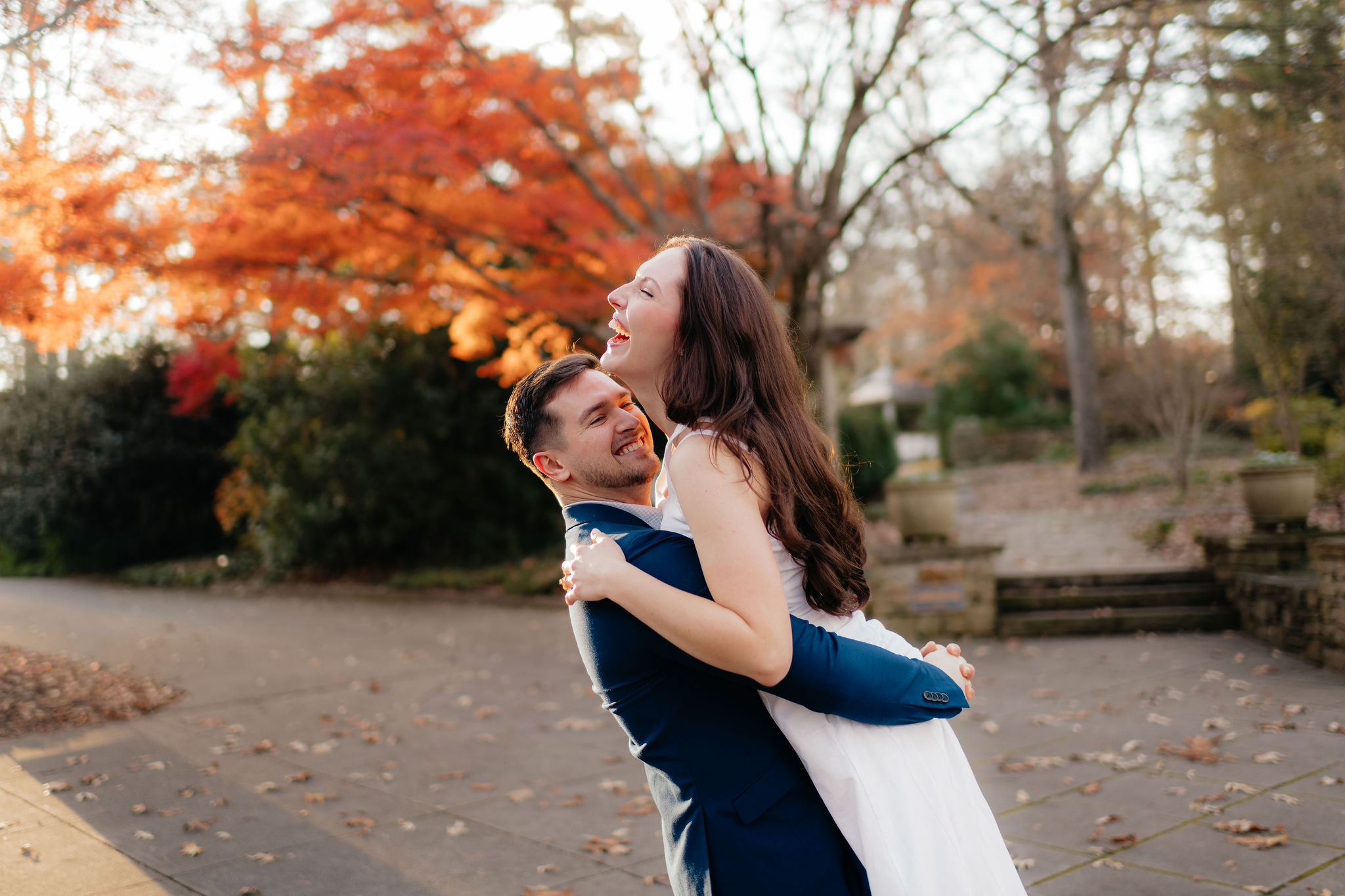 a couple laughs while spinning around near a fall maple tree at the birmingham botanical gardens in december, during their engagement photos with alabama wedding photographer sarah mismash