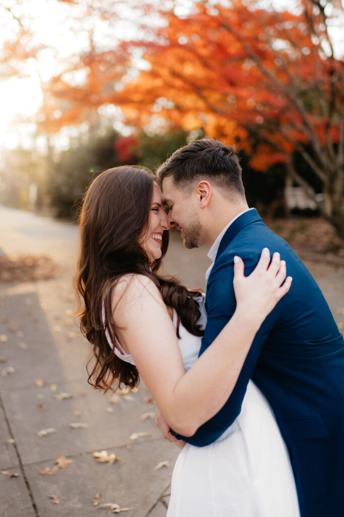 a couple kisses near a bright orange japanese maple tree during their december engagement photos at the birmingham botanical gardens with alabama engagement photographer sarah mismash