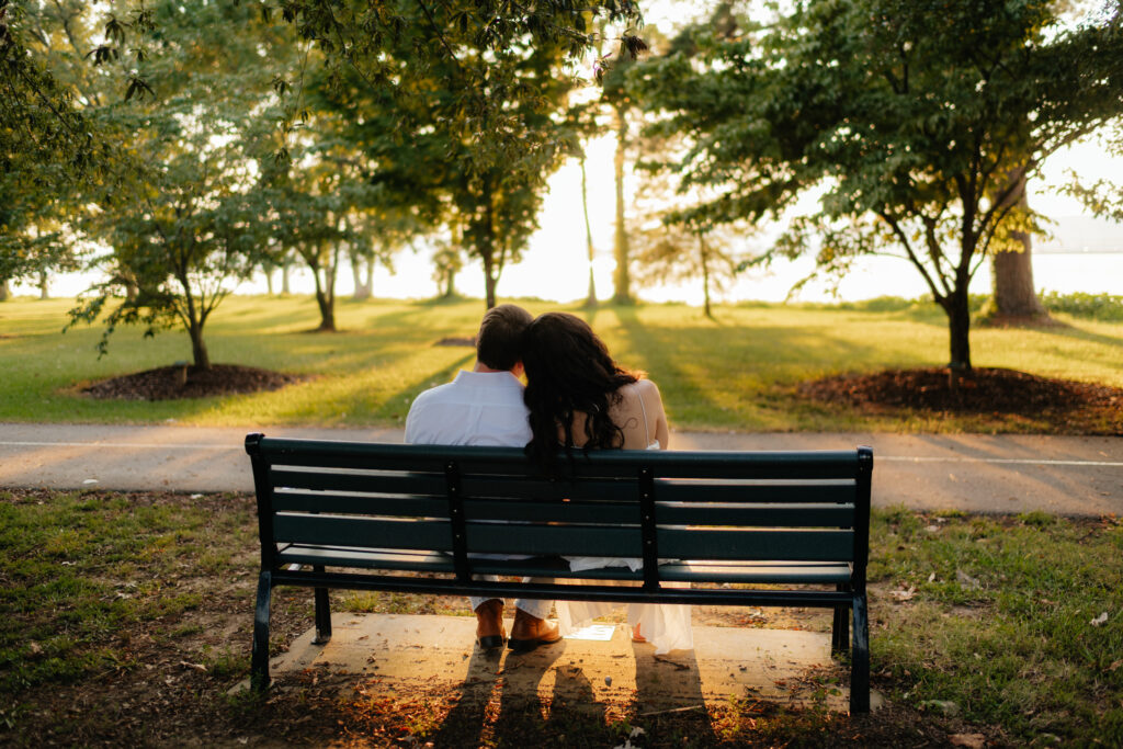a couple sits on a bench and watches the sunset during their engagement photos at Guntersville Lake with alabama wedding photographer Sarah Mismash