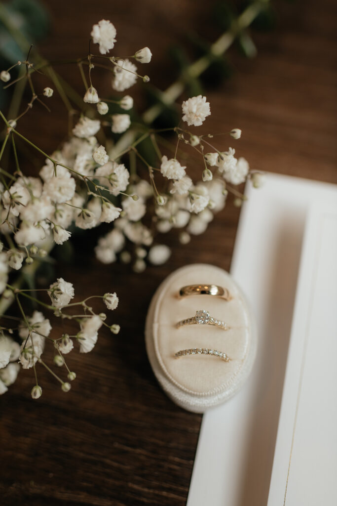 a wedding flat lay detail photo with three rings in a ring box and white florals. photographed by washington wedding photographer Sarah Mismash