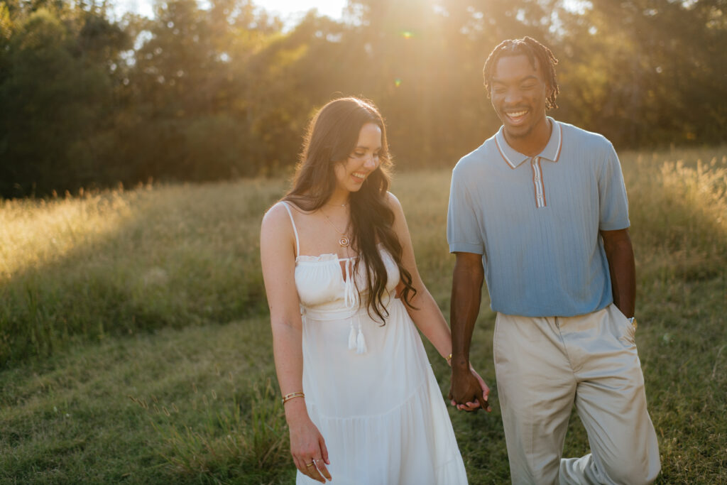 a couple walks through a field during their engagement photos with Olympia engagement photographer Sarah Mismash