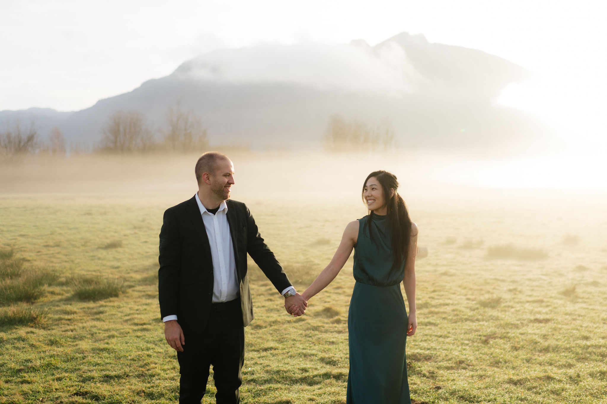 Couple holding hands in a field near Mount Si in Snoqualmie Washington during engagement photos — suit outfit idea for men's summer engagement photos