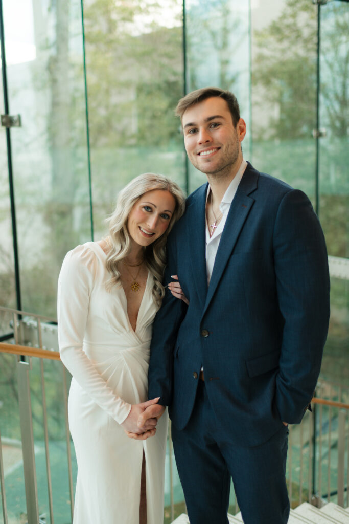 a couple stands near the large glass windows during their engagement photos at the Seattle Art Museum with seattle engagement photographer Sarah Mismash