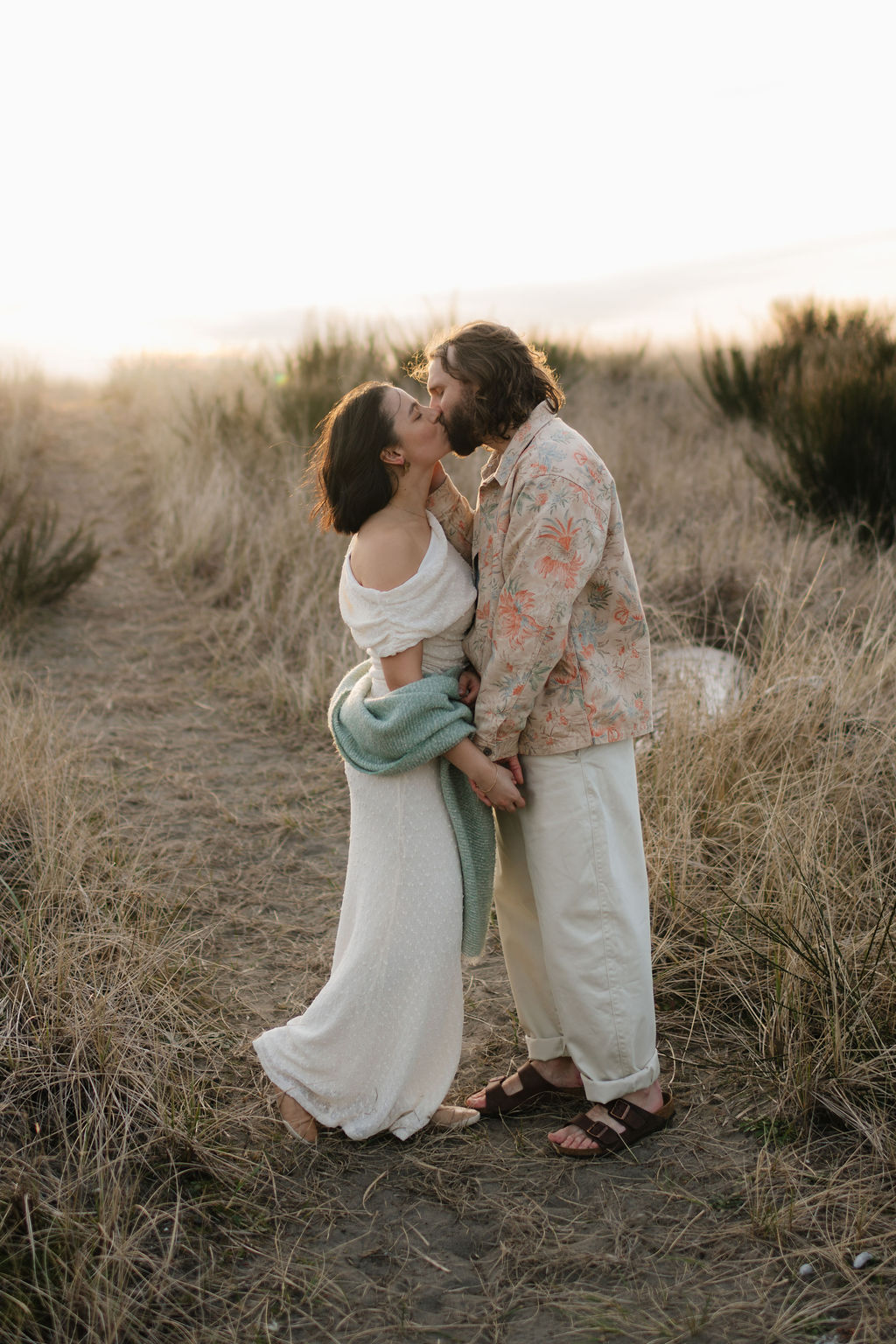 a couple kisses on the dunes at sunset at twin harbors state park during their engagement photos on the washington coast with Westport washington engagement photographer Sarah Mismash