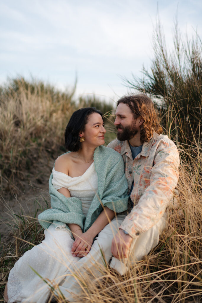 a couple smiles together during their engagement portraits on the washington coast
