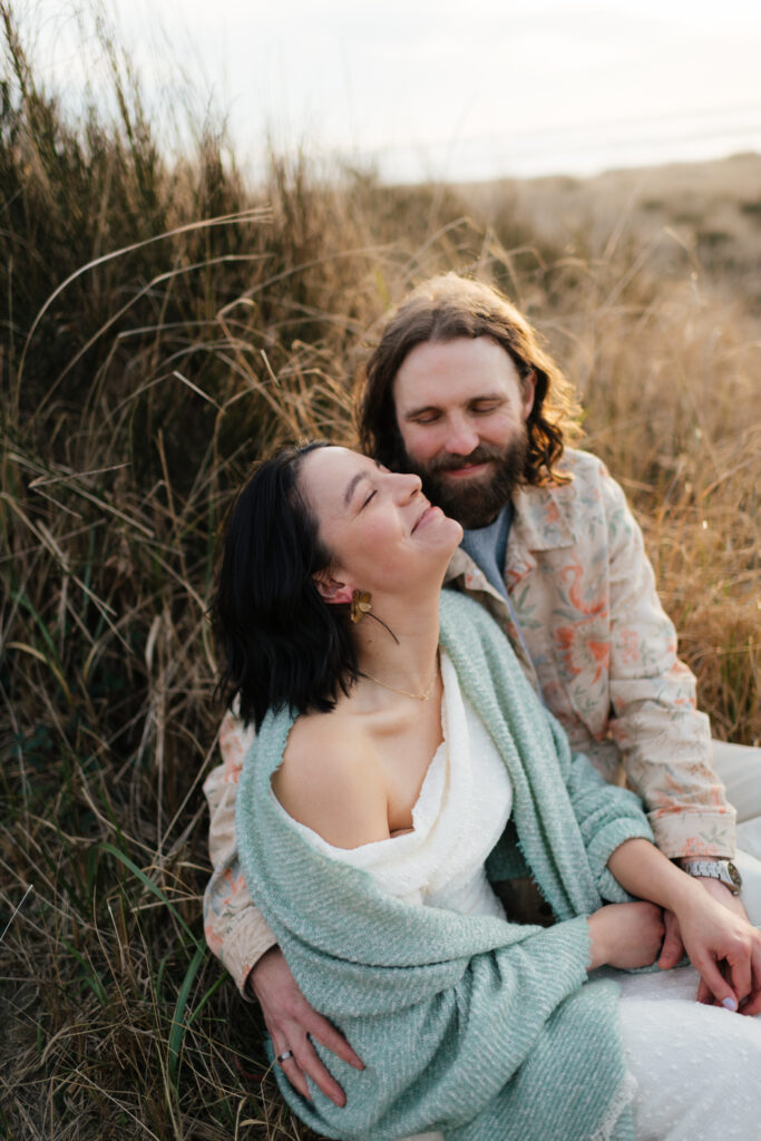 a couple laughs in the dunes at twin harbor state park during their engagement photography