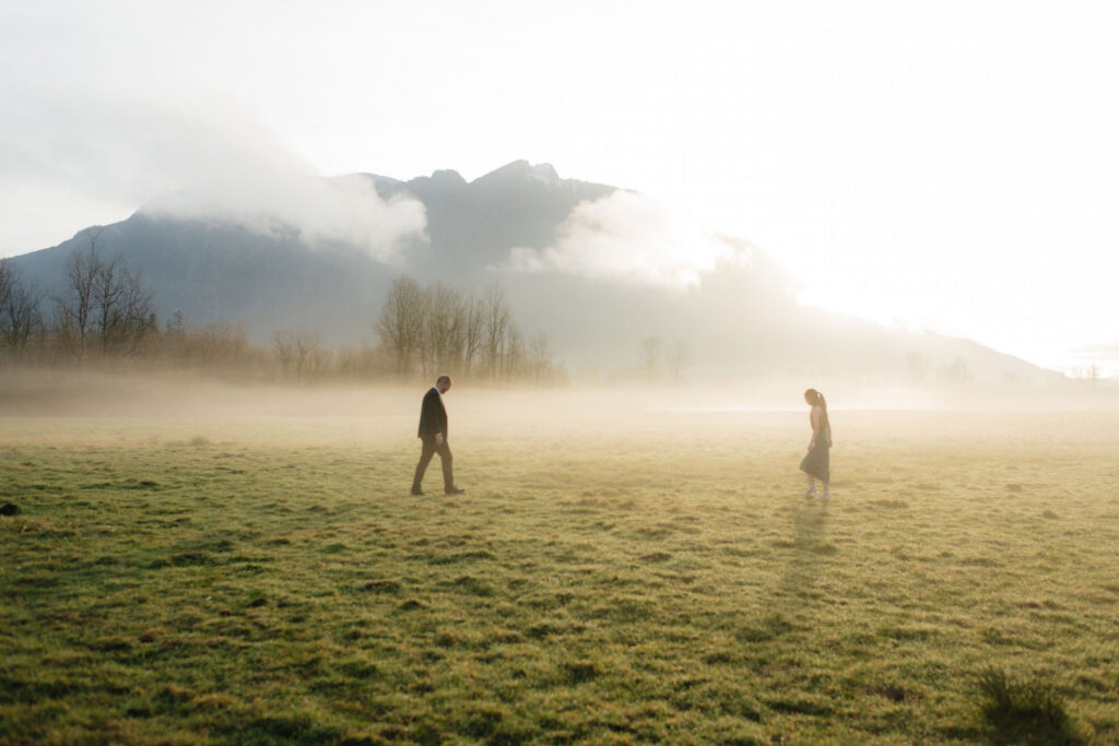 a couple walks through a field together during their engagement photos at the north bend elk fields near Mt Si in Snoqualmie, washington