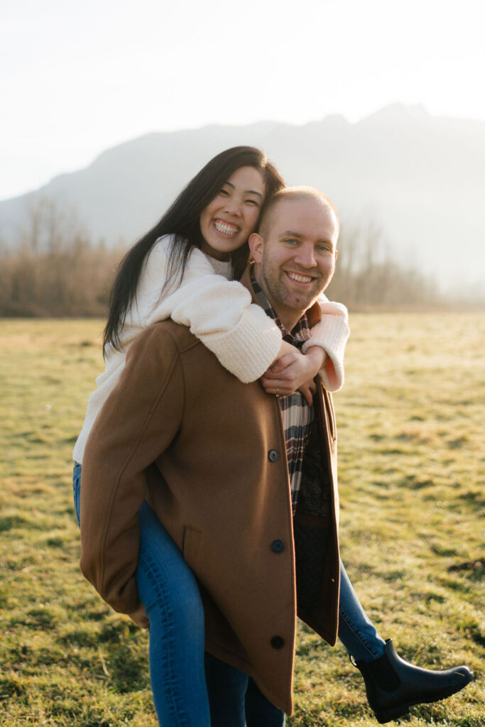 a man gives his fiance a piggy back ride during their winter engagement photos at the north bend elk fields near Snoqualmie Washington with north bend engagement photographer Sarah mismash