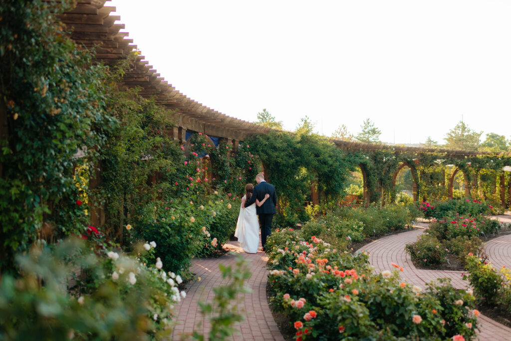 a couple walks through the rose garden at thanksgiving point during their engagement photos with utah county engagement photographer sarah mismash