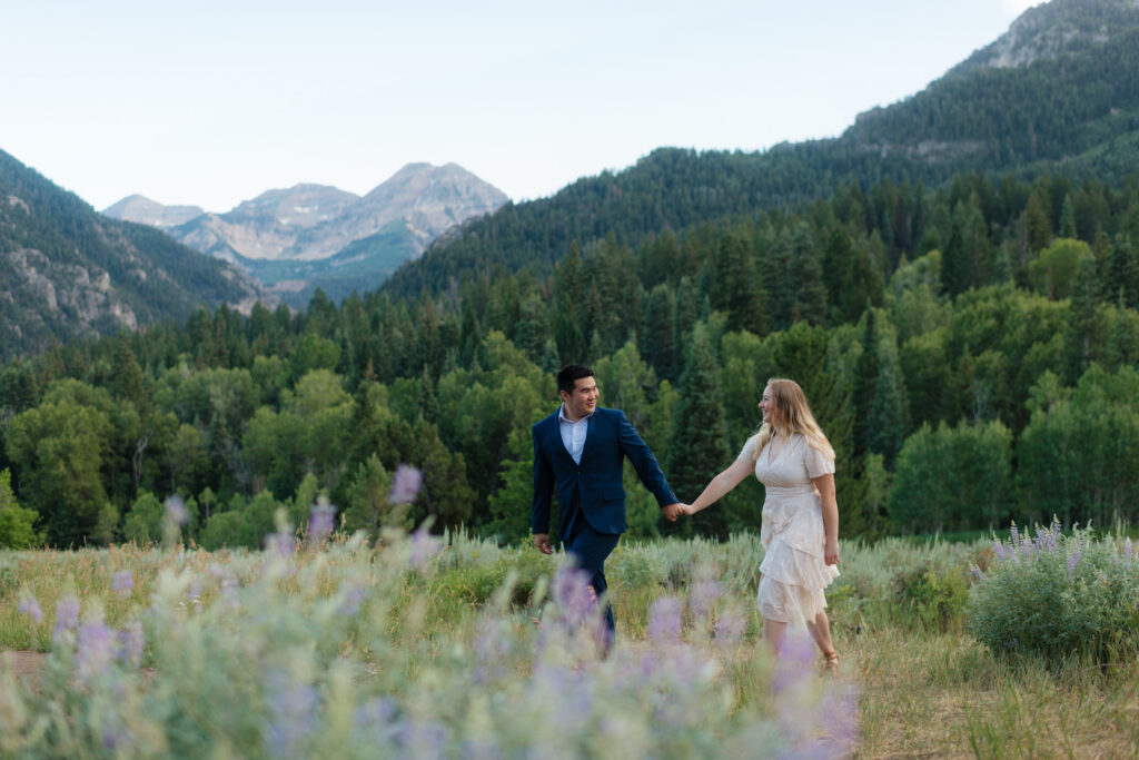 a couple walks through a field of lupines in remote american fork canyon, within view of mount timpanogas during their engagement photos with utah engagement photographer sarah mismash photography