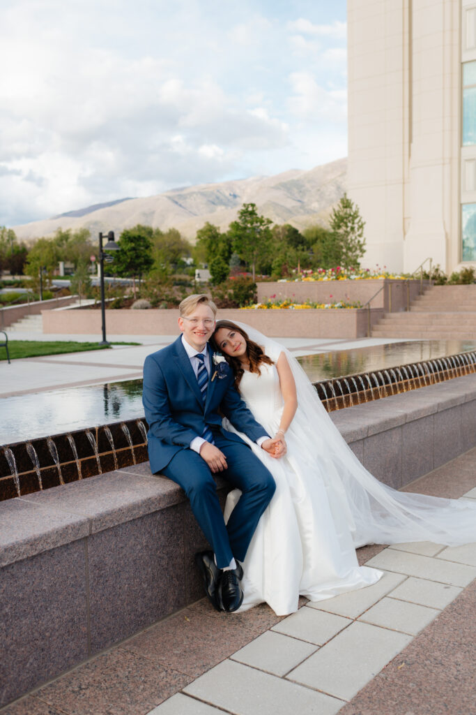 a bride and groom sit together at the fountain in front of the layton utah temple before their sealing