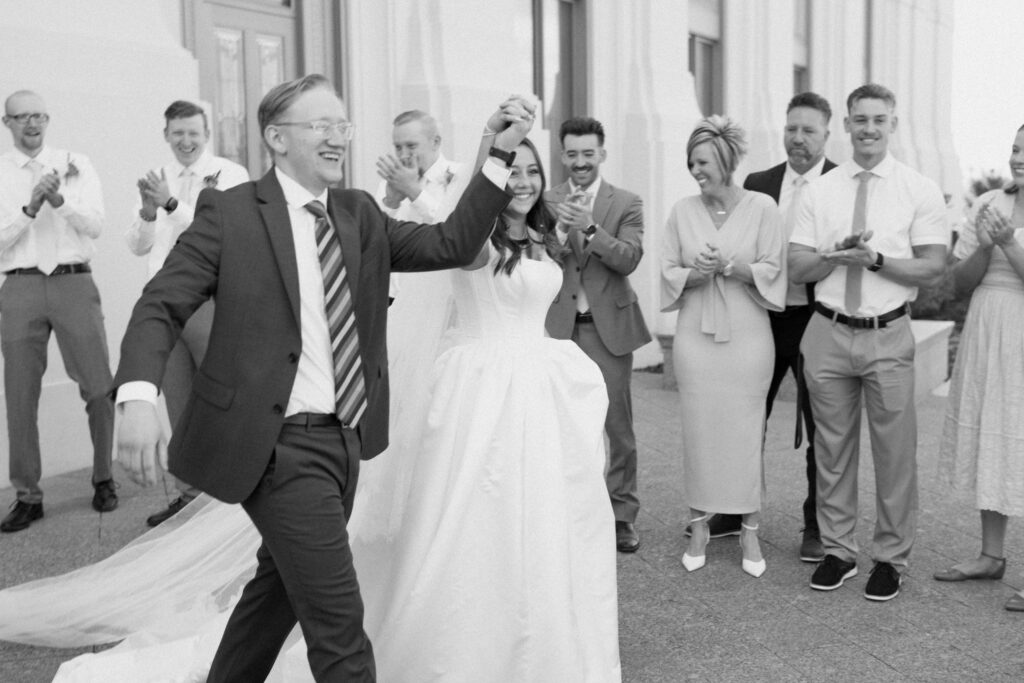 a couple cheers while exiting the layton utah temple after their sealing on their wedding day