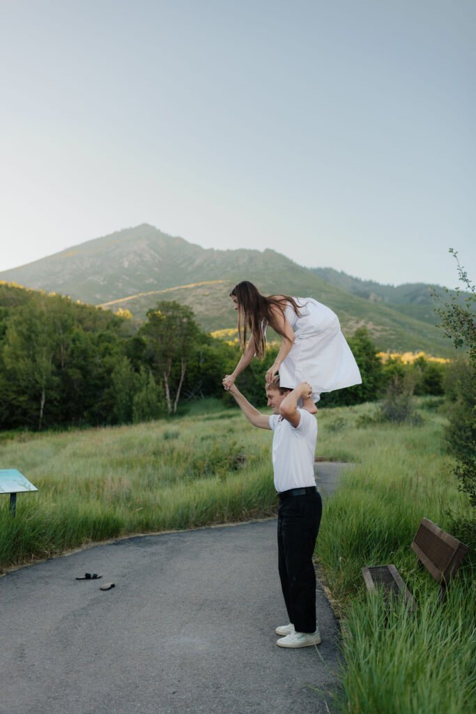 a bride stands on her fiance's shoulders during their summer engagment photos in the alpine loop at american fork canyon and provo canyon, photographed by utah county engagement photographer sarah mismash