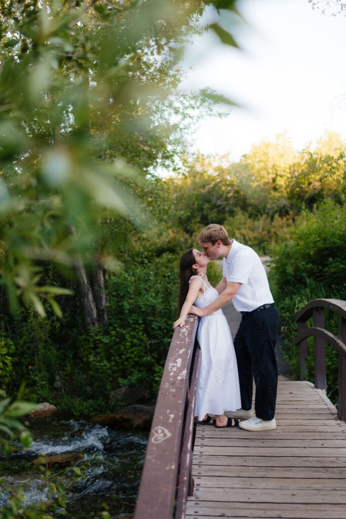 a couple kisses on a bridge during their summer engagment photos in the alpine loop at american fork canyon and provo canyon, photographed by utah county engagement photographer sarah mismash