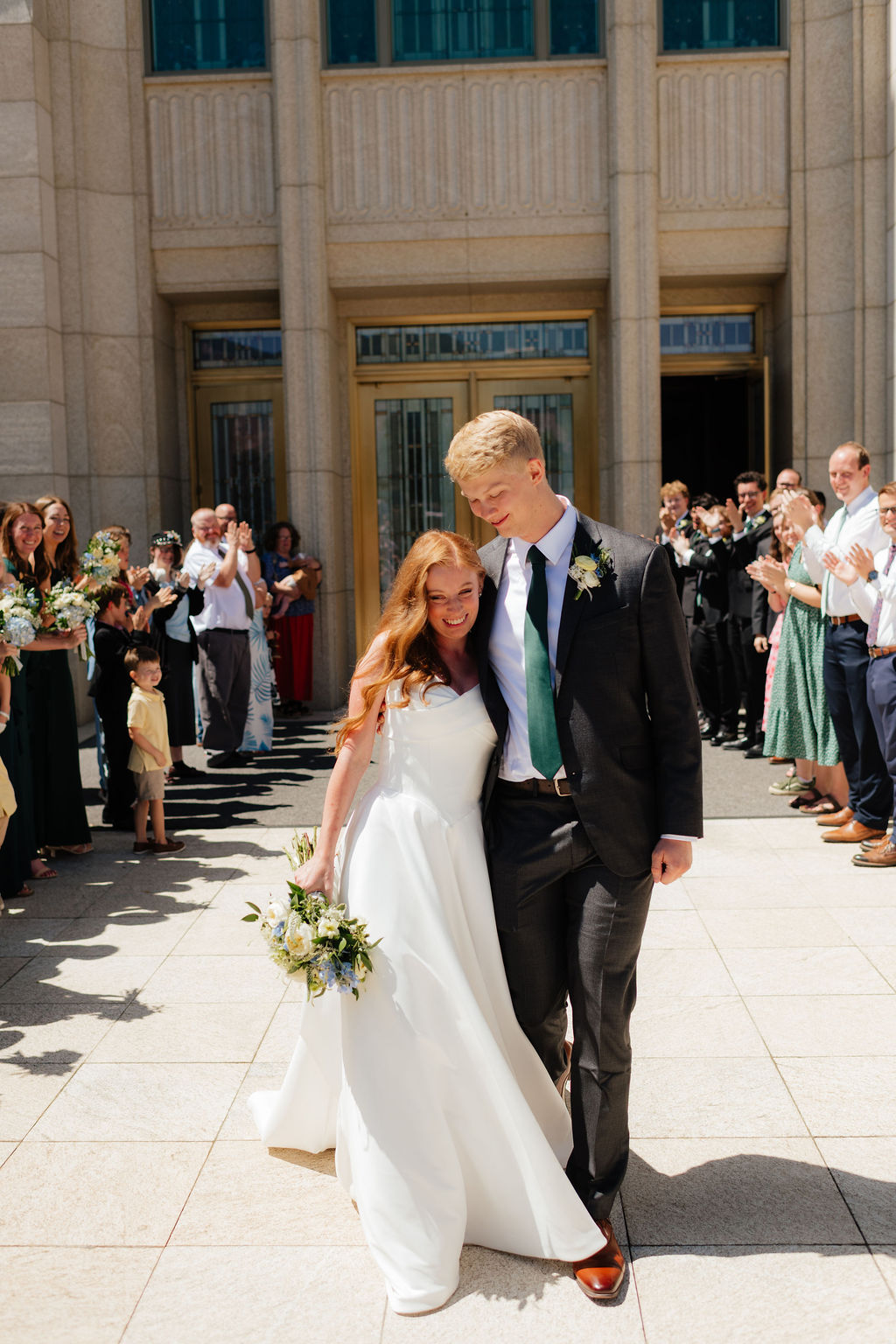 a bride and groom walk through their friends and family during their temple exit during an august wedding photgraphed on the ogden temple grounds by utah wedding photographer sarah mismash