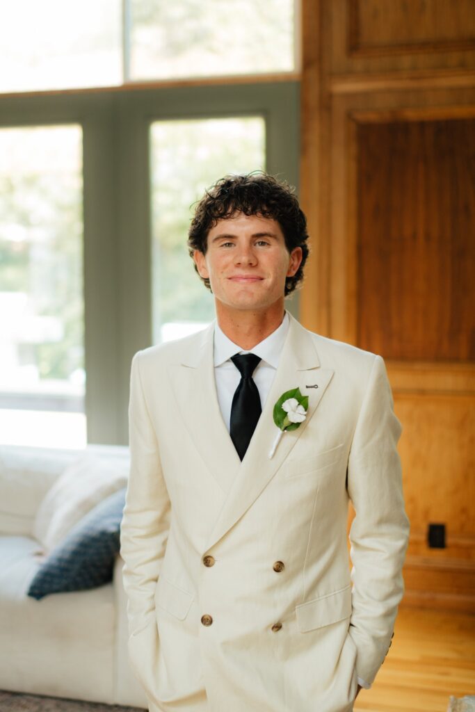 Groom in cream suit standing indoors on his wedding morning