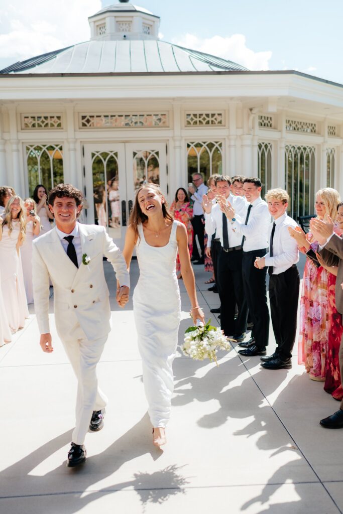 newlyweds walk hand in hand through a crowd of cheering guests just after their September wedding ceremony at the Provo City Center Temple.