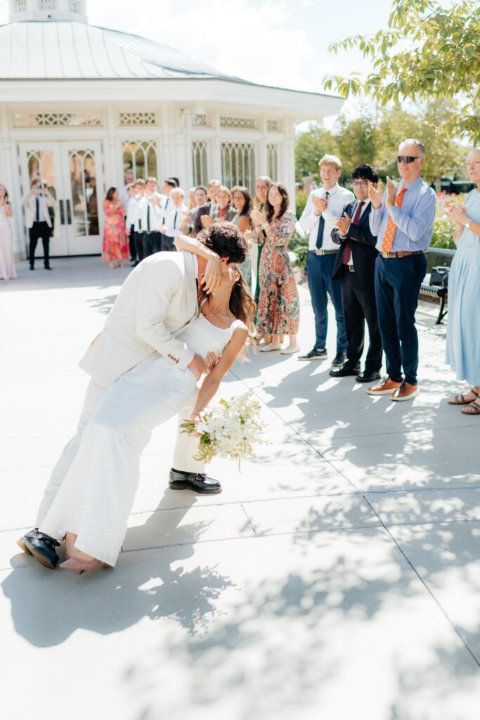 Wedding guests clap and celebrate as the couple exits the Provo City Center Temple grounds after their September wedding. bride and groom dip kiss
