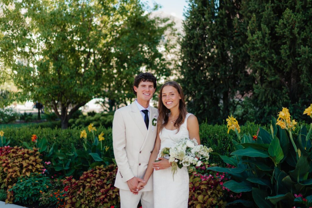 The newlyweds pose among the temple's garden flowers on their September wedding day, photographed by a Provo City Center Temple wedding photographer sarah mismash