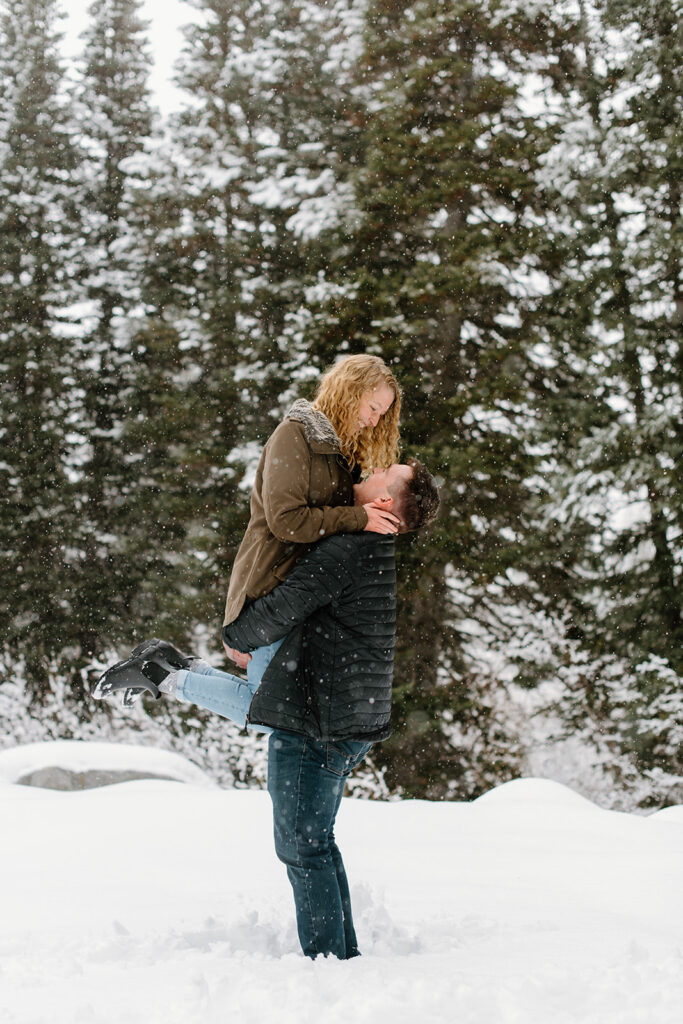 a couple kisses in the falling snow during a snowy winter engagement session in big cottonwood canyon