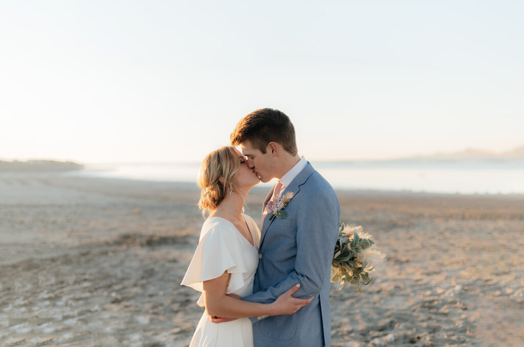 a couple kisses at sunset during their snowy backup wedding portrait location at antelope island in february